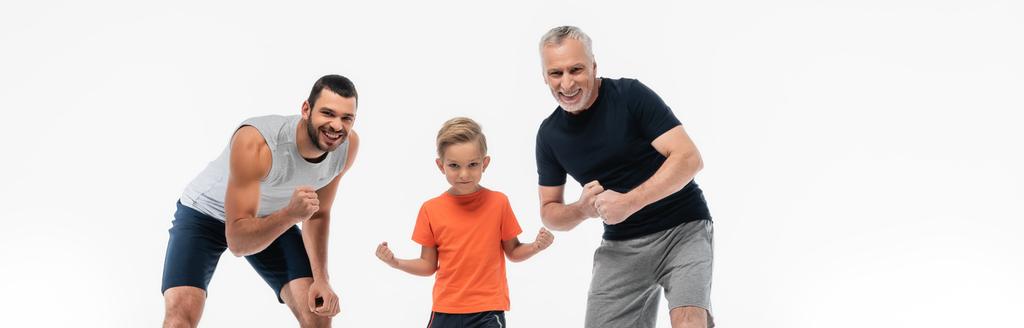 niño con padre y abuelo en ropa deportiva sonriendo a la cámara mientras demuestra fortalezas aisladas en blanco, pancarta - Foto, Imagen