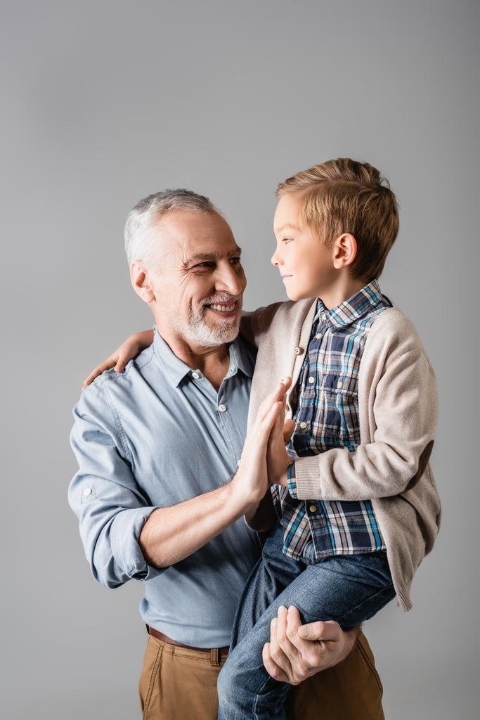 sorridente nonno che dà il cinque al nipote mentre lo tiene isolato sul grigio - Foto, immagini