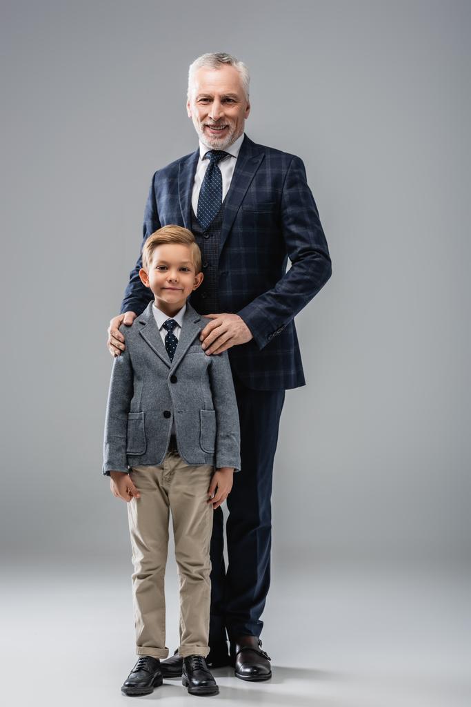 glücklicher Geschäftsmann umarmt Schultern seines Enkels, während er auf grau steht - Foto, Bild