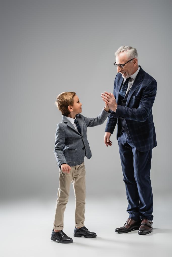 gelukkig volwassen zakenman geven high vijf naar kleinzoon op grijs - Foto, afbeelding