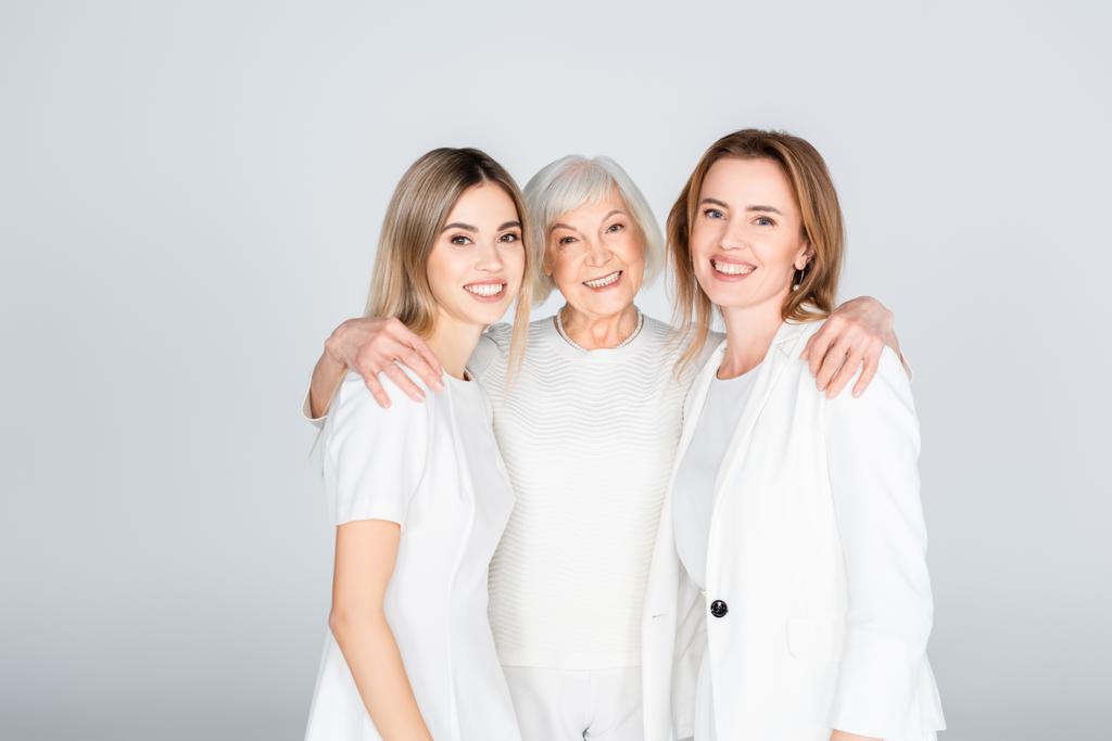 three generation of cheerful women smiling while looking at camera and hugging isolated on grey - Photo, Image
