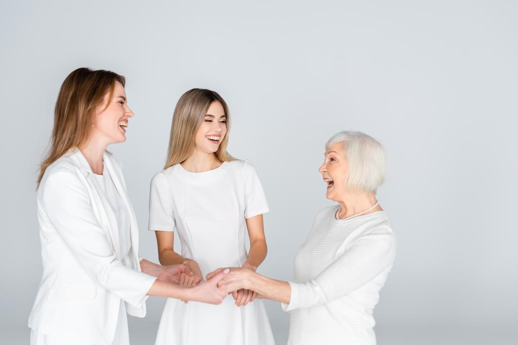 tre generazioni di donne gioiose sorridenti mentre si tengono le mani isolate sul grigio - Foto, immagini