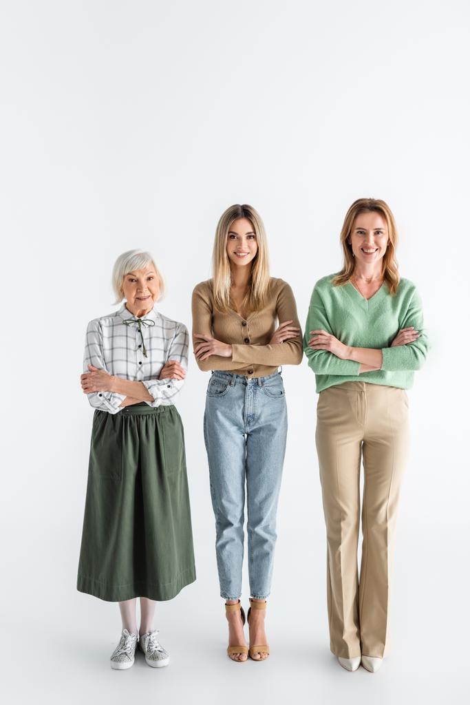 Полная длина трех поколений счастливых женщин улыбаясь стоя со скрещенными руками на белом - Фото, изображение