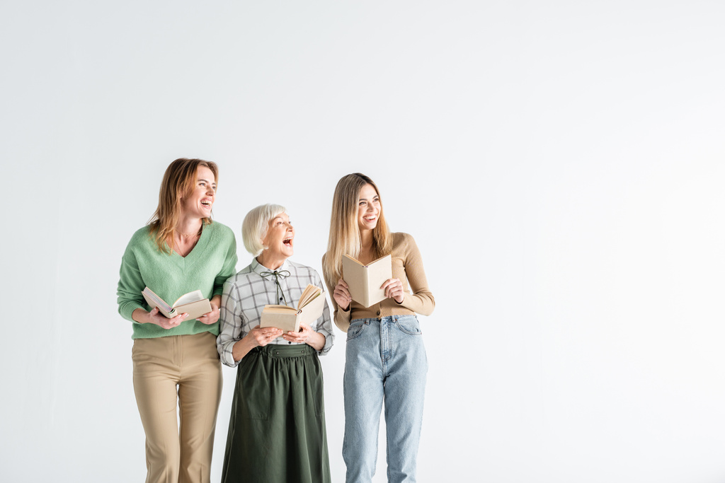 tre generazioni di donne felici che tengono libri e distolgono lo sguardo dal bianco - Foto, immagini