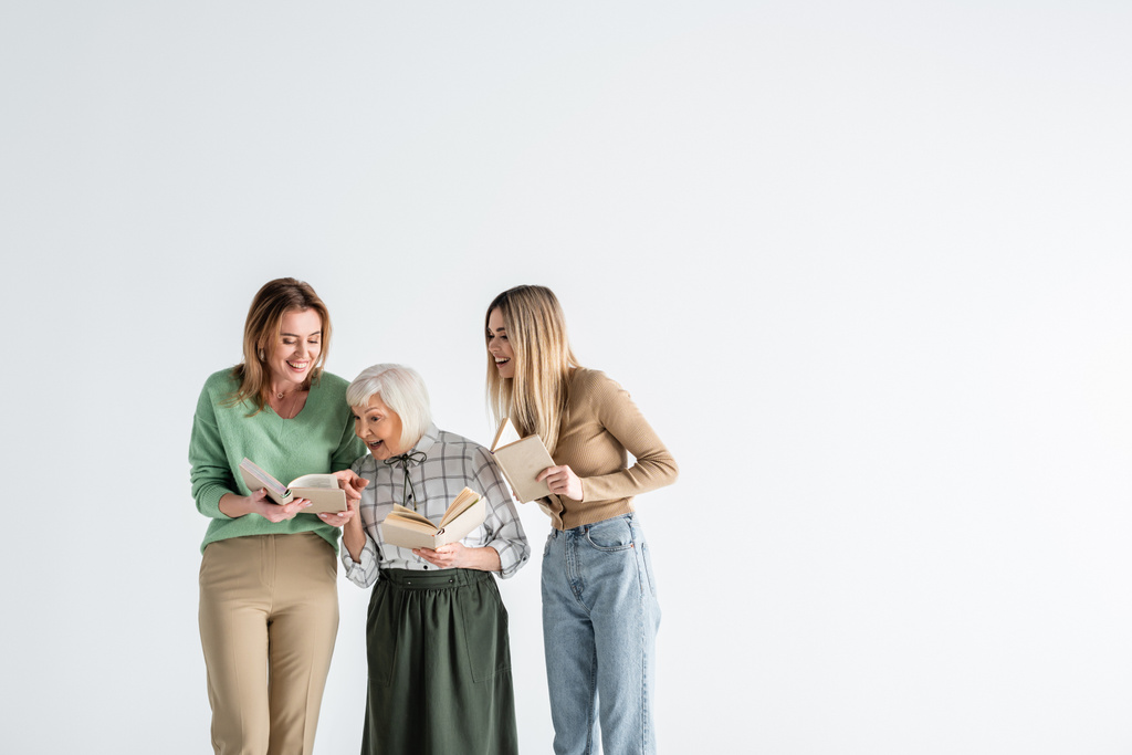 három generáció boldog nők gazdaság könyvek és mosolygó elszigetelt fehér - Fotó, kép