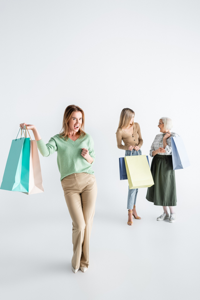 full length of happy woman with shopping bags near daughter and senior mother on blurred white background - Photo, Image