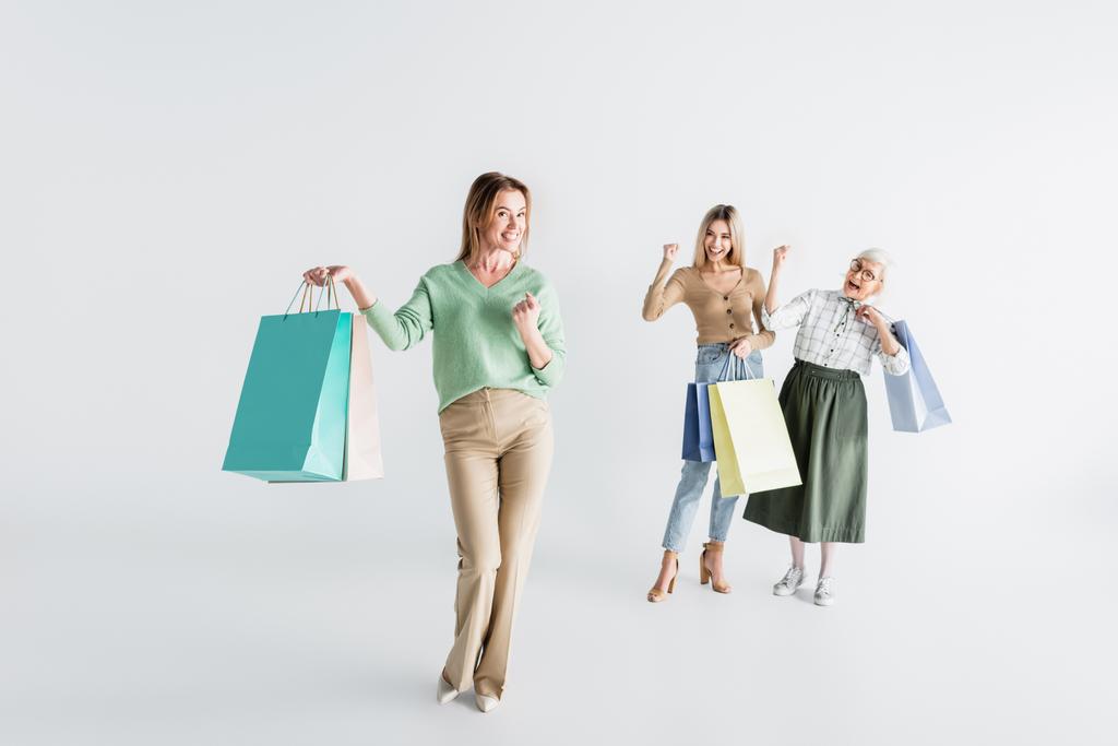 comprimento total da mulher feliz com sacos de compras perto da filha e da mãe sênior no fundo branco borrado - Foto, Imagem