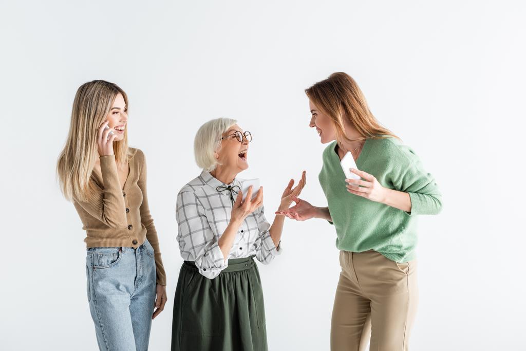 három generációs csodálkozó nők gazdaság okostelefonok és nézik egymást elszigetelt fehér - Fotó, kép