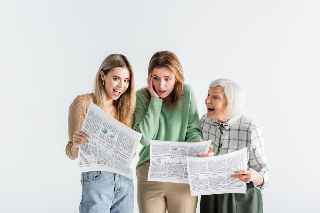 τρεις γενιές έκπληκτων γυναικών που διαβάζουν εφημερίδες απομονωμένες στα λευκά - Φωτογραφία, εικόνα
