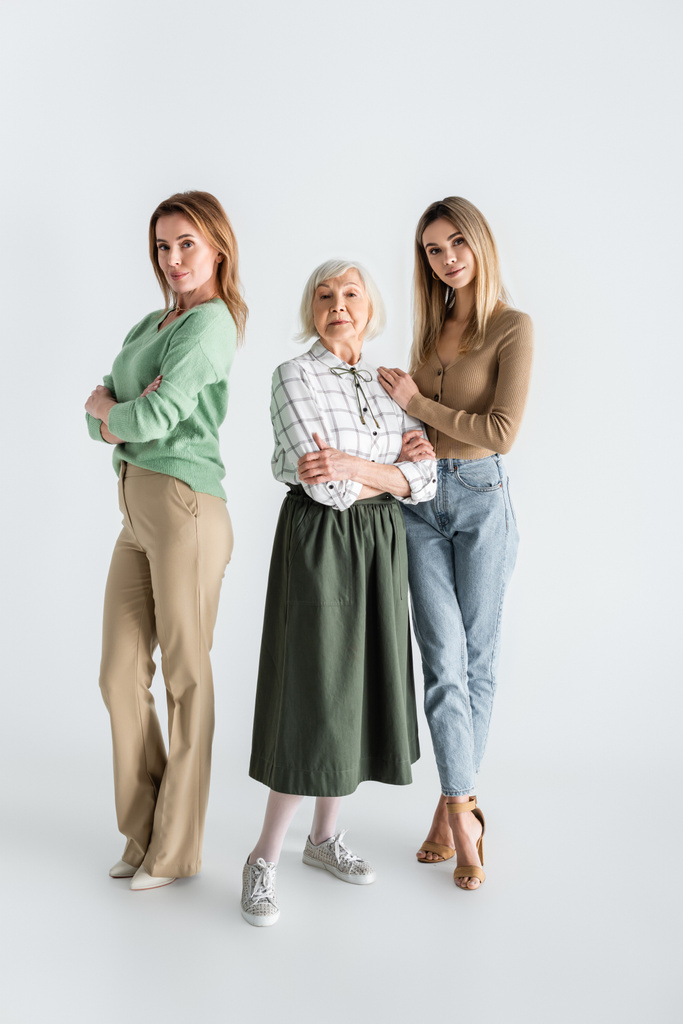 longitud completa de tres generaciones de mujeres mirando a la cámara y posando en blanco - Foto, imagen
