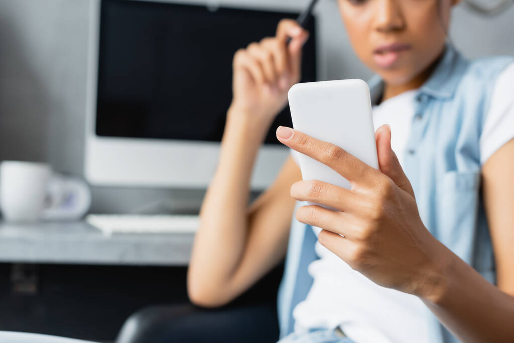 vue partielle d'un pigiste afro-américain tenant un smartphone à la maison, fond flou - Photo, image