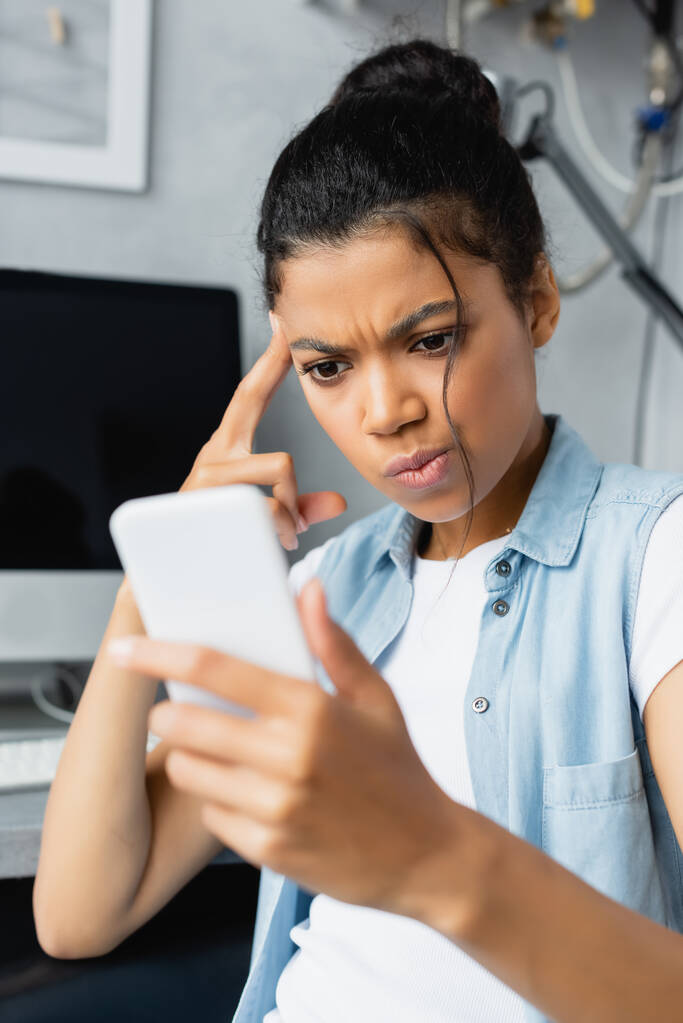réfléchi afro-américain pigiste tenant smartphone à la maison, flou au premier plan - Photo, image