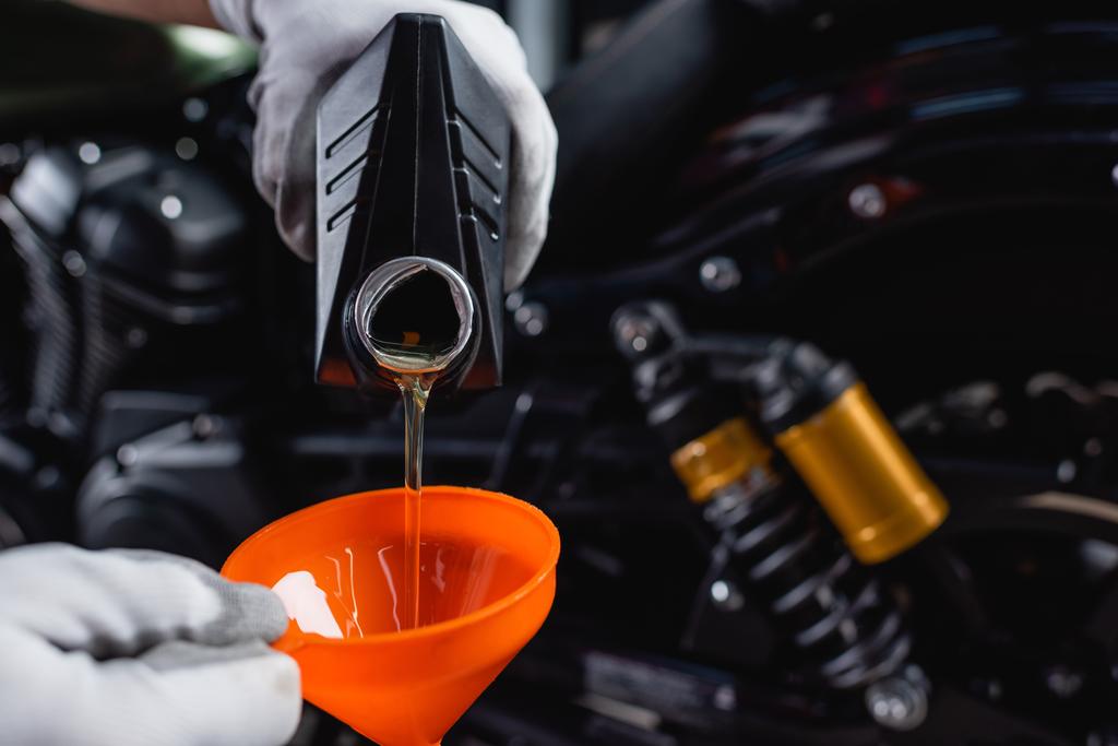 Teilansicht des Mechanikers in Handschuhen, der Motoröl aus der Flasche in den Trichter gießt - Foto, Bild