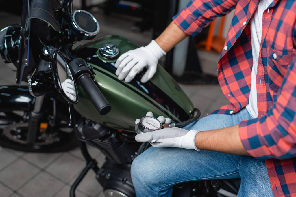 обрезанный вид техника в перчатках, измеряющих давление воздуха в шинах мотоцикла с помощью манометра - Фото, изображение
