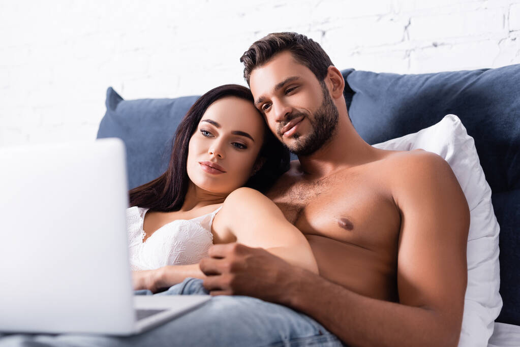 Nuori seksikäs pari etsii hämärtynyt kannettava etualalla makuuhuoneessa - Valokuva, kuva