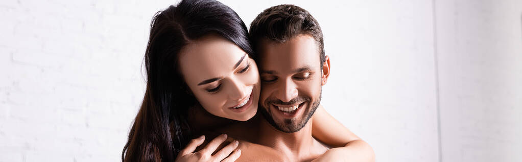 улыбающаяся брюнетка обнимает мужчину без рубашки в помещении, плакат - Фото, изображение