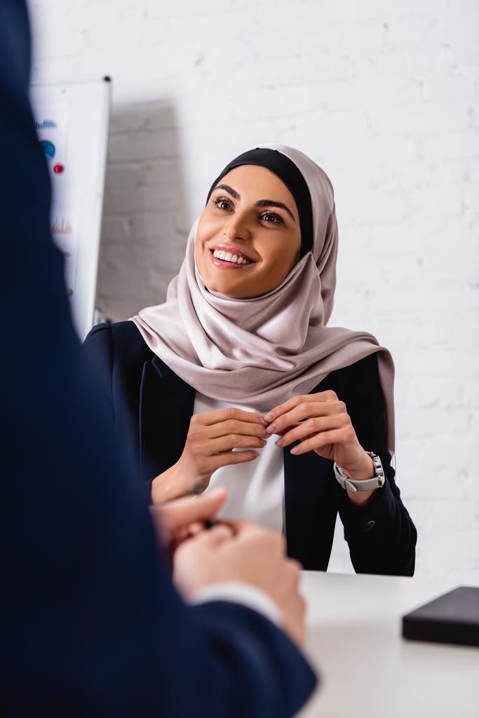 счастливая арабская бизнесвумен смотрит на переводчика на размытом переднем плане - Фото, изображение