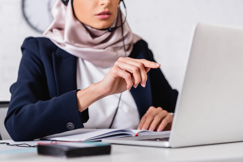 Ausgeschnittene Ansicht des arabischen Dolmetschers, der mit dem Finger in der Nähe von Laptop und digitalem Übersetzer auf verschwommenem Vordergrund zeigt - Foto, Bild