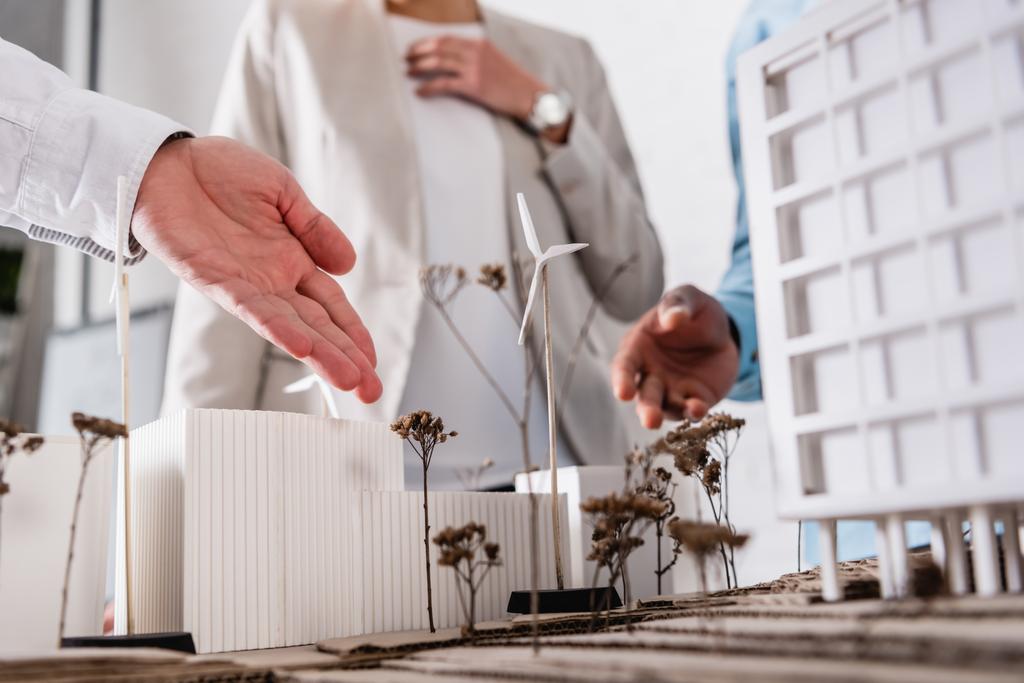 cropped view of businessman pointing at alternative energy station near building model and multiethnic partners on blurred background - Photo, Image