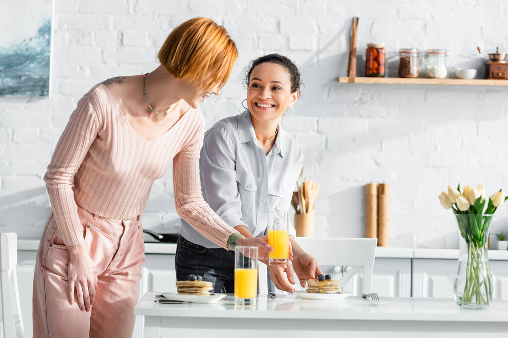 vidám, fajok közötti leszbikus pár, akik reggelit szolgálnak fel a konyhában - Fotó, kép