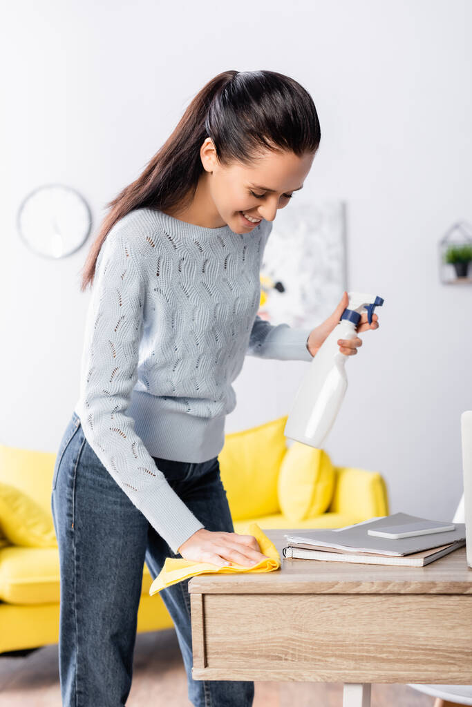 giovane casalinga in possesso di detergente spray e strofinare tavolo con straccio - Foto, immagini