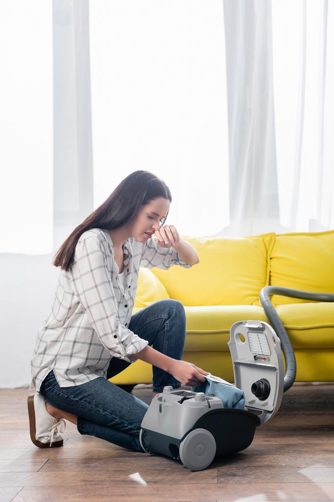 allergic woman wiping nose while changing dust bag in vacuum cleaner - Photo, Image