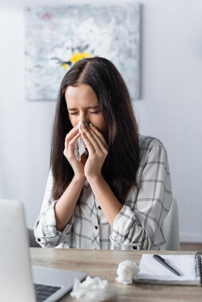 freelancer estornuda en servilleta de papel mientras sufre de alergia cerca de la computadora portátil en primer plano borroso - Foto, Imagen