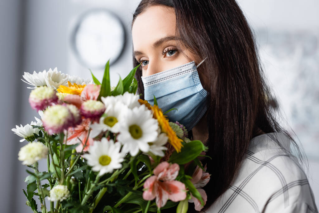 mujer alérgica joven en máscara médica con ramo de flores en casa - Foto, Imagen