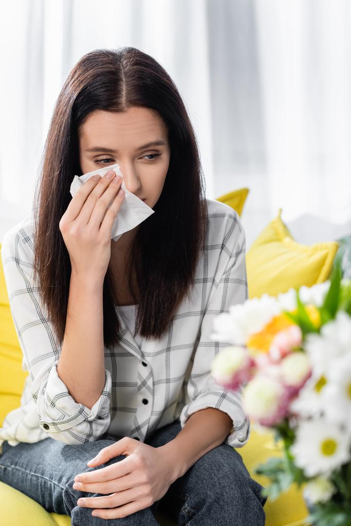 allergische vrouw veegt tranen in de buurt van bloemen op wazig voorgrond - Foto, afbeelding