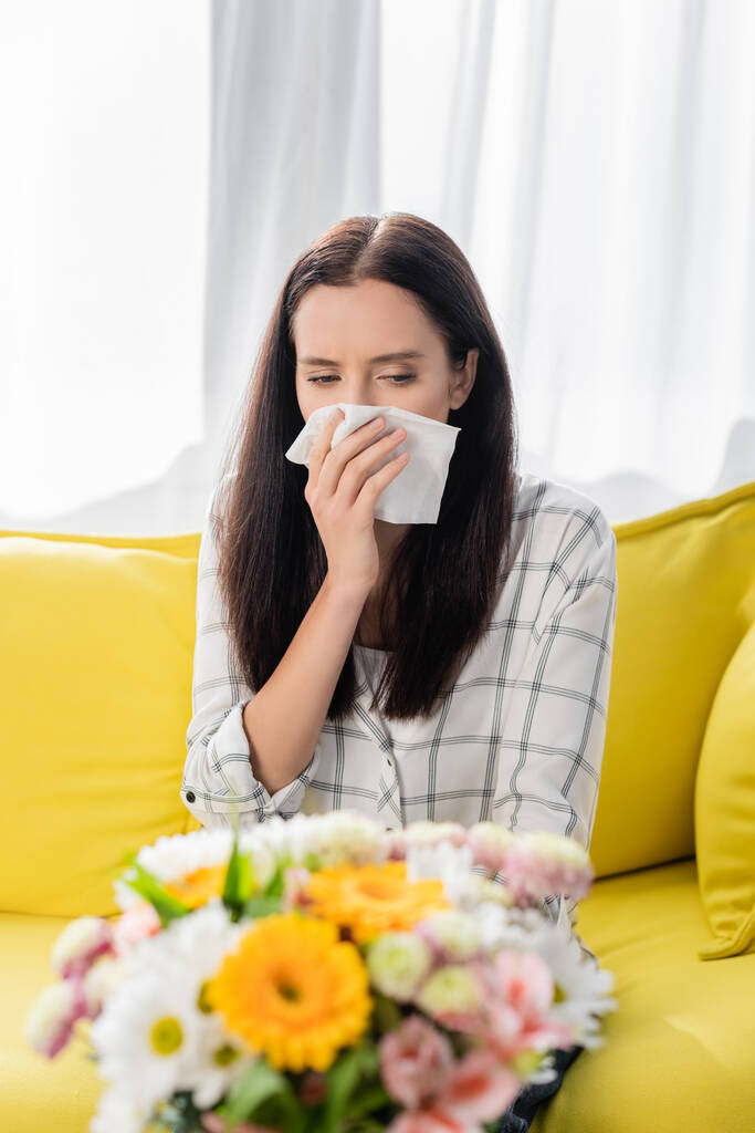 allergic woman wiping nose with paper napkin near bouquet on blurred foreground - Photo, Image