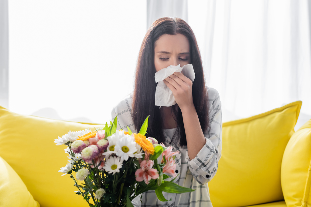 allerginen nainen pyyhkimällä nenän paperilla lautasliina istuessaan lähellä kukkia - Valokuva, kuva