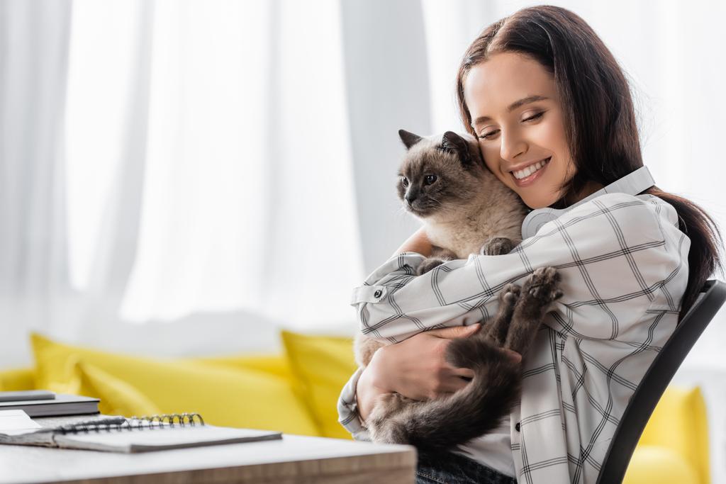 happy freelance hugging cat while sitting at table, blurred front ground - Фото, изображение