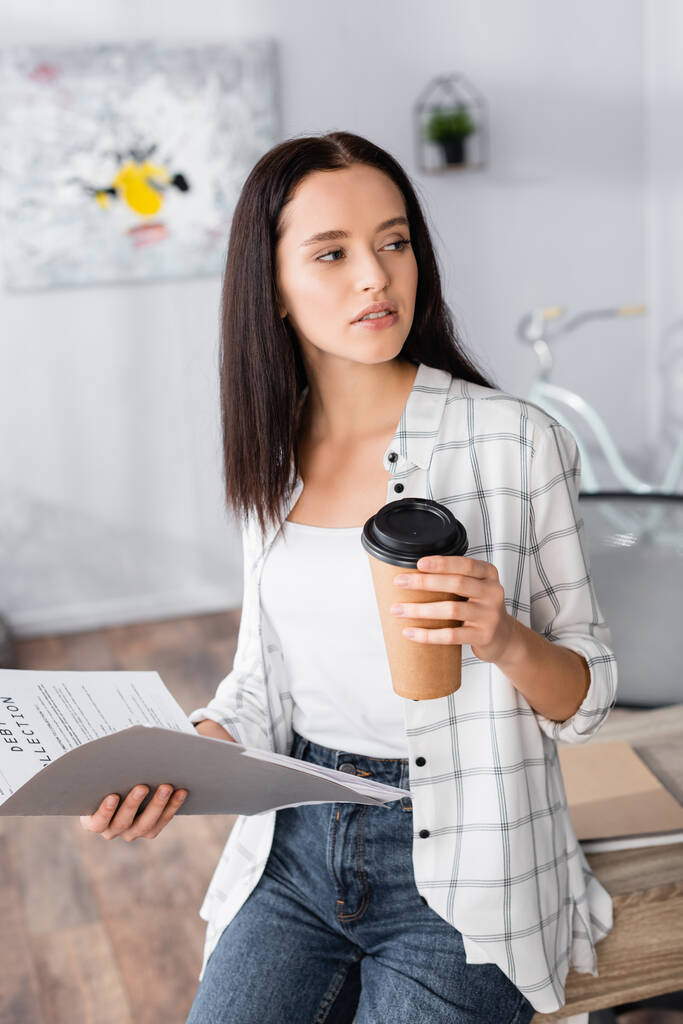 fiatal szabadúszó néz félre, miközben kezében papír mappa és kávé menni - Fotó, kép
