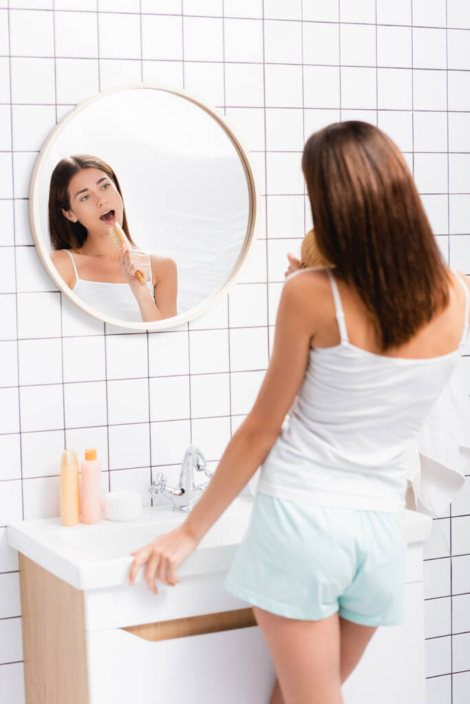 giovane donna in pantaloncini bianchi e canto singoletto con spazzola in bagno - Foto, immagini