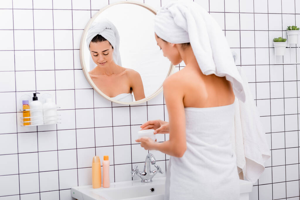 Nuori nainen valkoinen pyyhe pään avaaminen kosmeettinen kerma kylpyhuoneessa - Valokuva, kuva