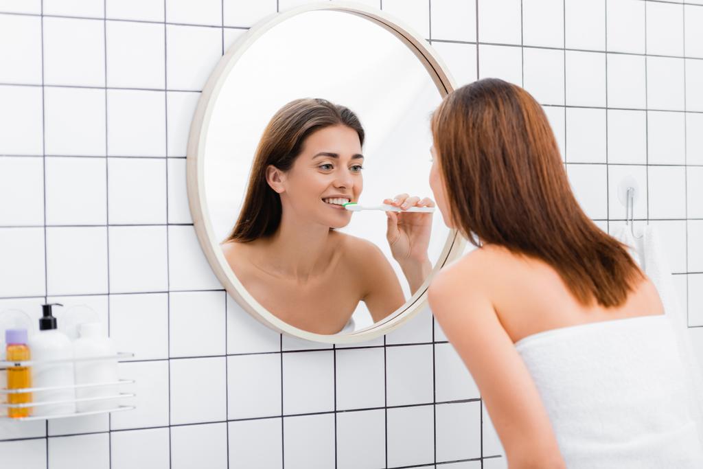 fiatal nő néz tükörbe, miközben fogat mos a fürdőszobában - Fotó, kép
