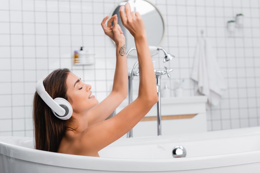uśmiechnięta kobieta kąpie się podczas słuchania muzyki w słuchawkach bezprzewodowych - Zdjęcie, obraz