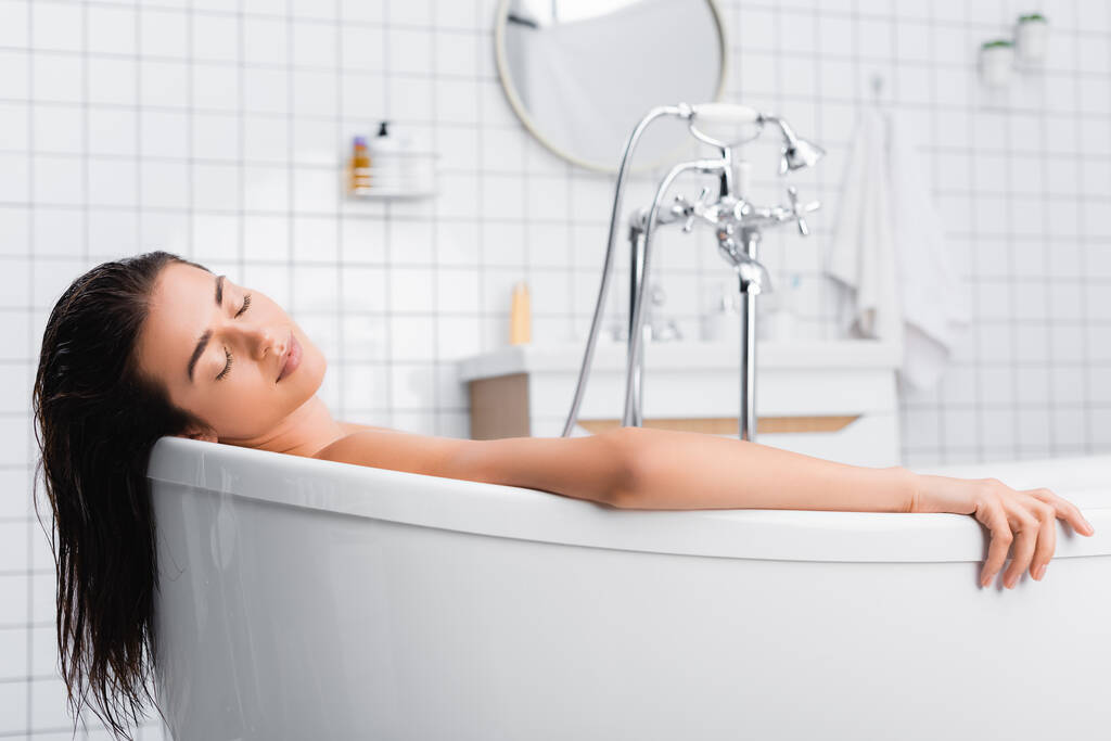 jeune femme avec les yeux fermés relaxant tout en prenant un bain à la maison - Photo, image