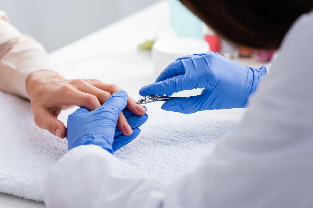 partial view of manicurist holding cuticle nipper near hand of woman, blurred foreground - Photo, Image