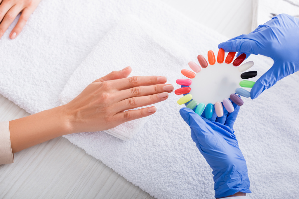 partial view of manicurist holding samples of colorful artificial nails near hand of client - Photo, Image