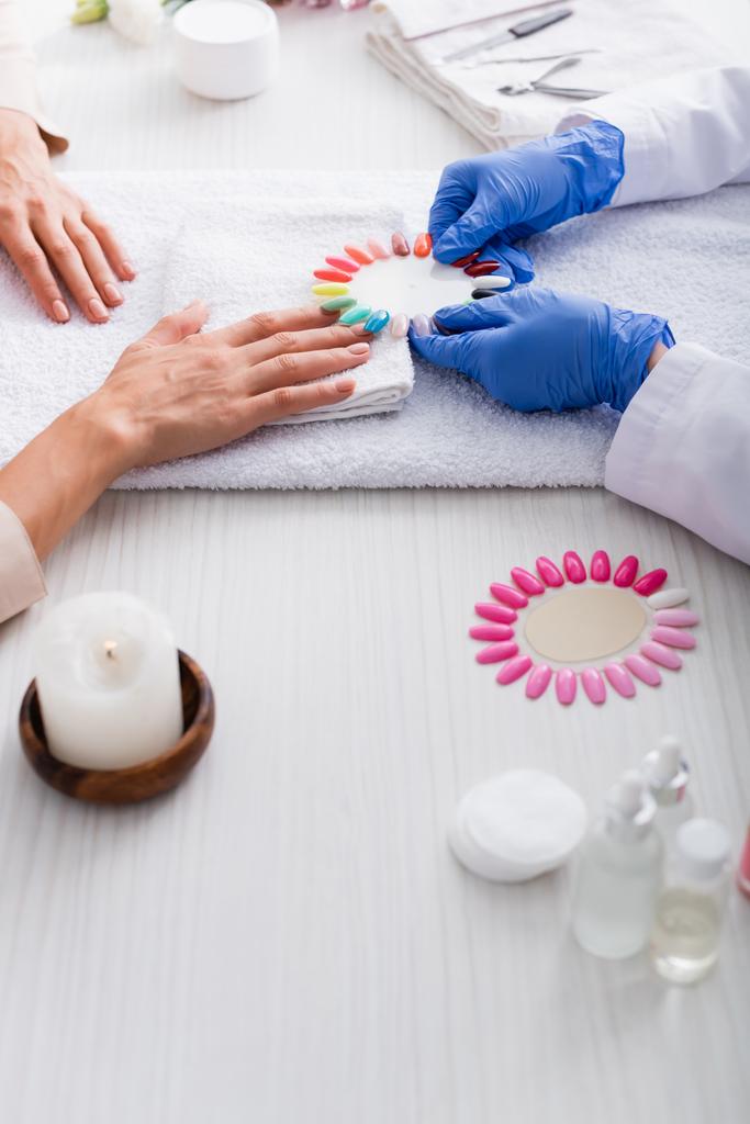 cropped view of manicurist holding set of artificial nails near client and manicure supplies on blurred foreground - Photo, Image