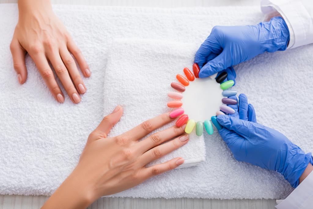 cropped view of manicurist holding palette of multicolored fake nails near client  - Photo, Image