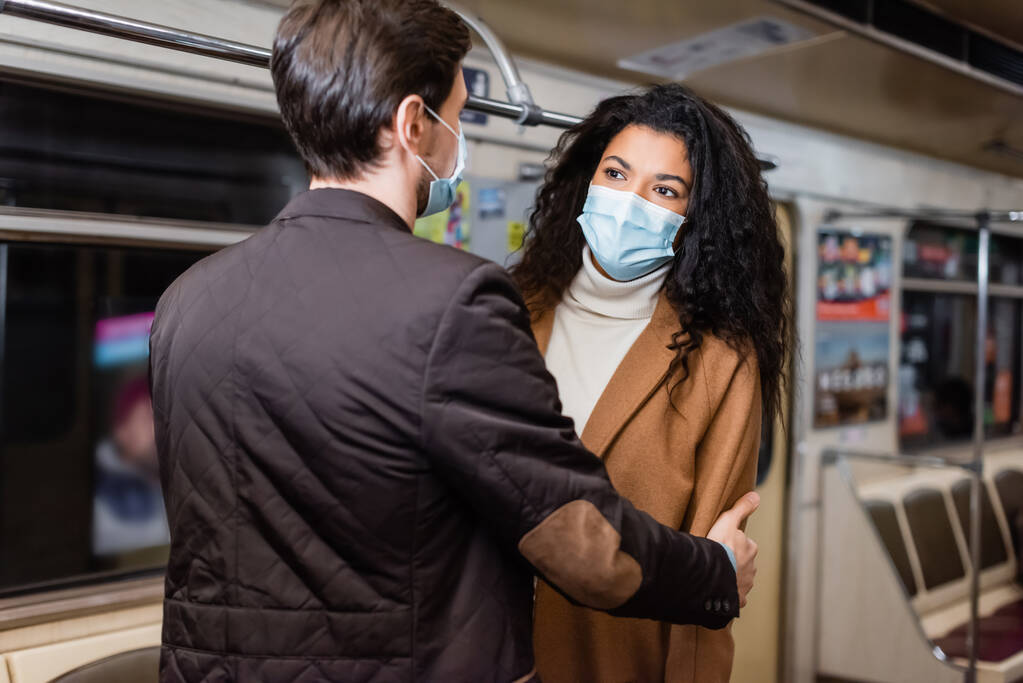 地下鉄の医療マスクを着たアフリカ系アメリカ人の彼女を抱きしめる男の姿  - 写真・画像