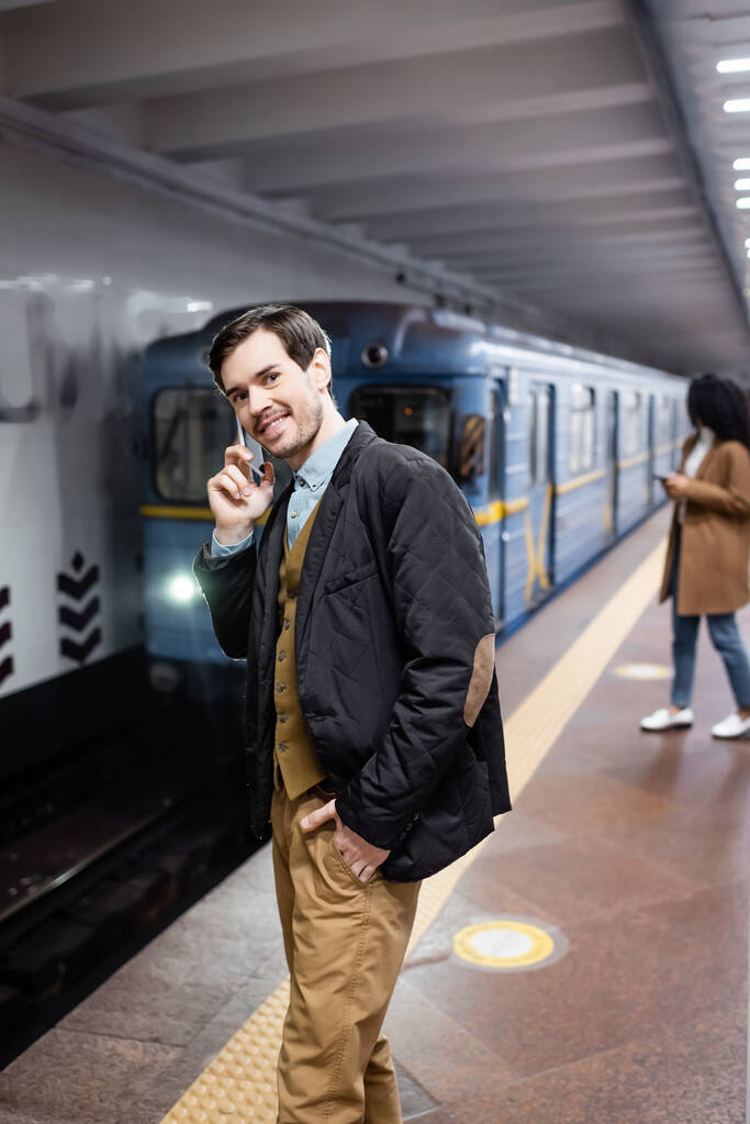 счастливый человек разговаривает на смартфоне рядом с африканской американкой и универсал метро на размытом фоне  - Фото, изображение