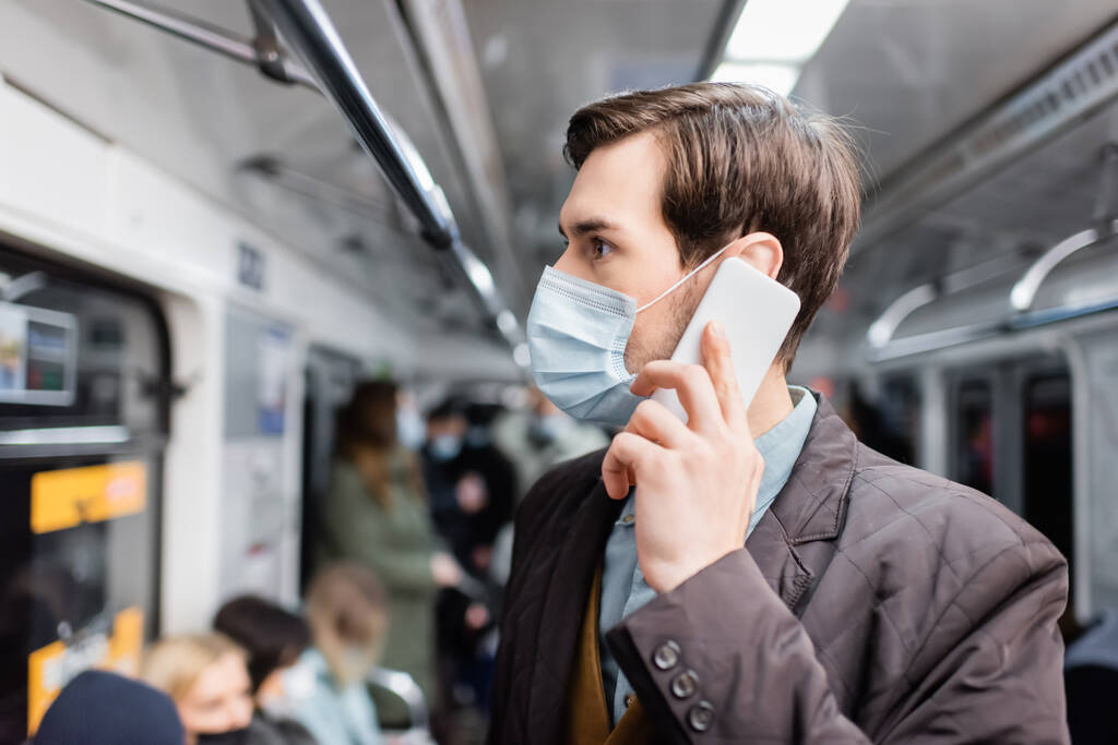 uomo in maschera medica parlare su smartphone mentre in piedi in carro della metropolitana  - Foto, immagini