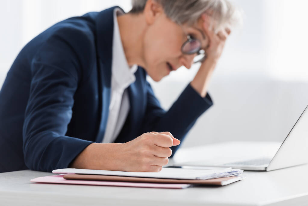 zamazana bizneswoman w średnim wieku z zaciśniętą pięścią cierpiąca na ból głowy w biurze - Zdjęcie, obraz