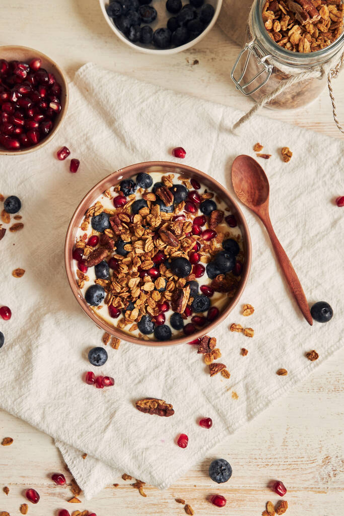 Een verticale shot heerlijke gezonde veganistische granola met pecannoten in een fruitige kom met yoghurt op een witte tafel - Foto, afbeelding