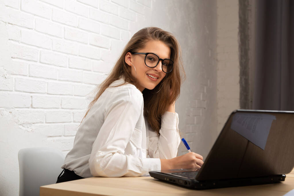belle jeune femme dans des lunettes à la table avec un ordinateur portable dans le bureau - Photo, image