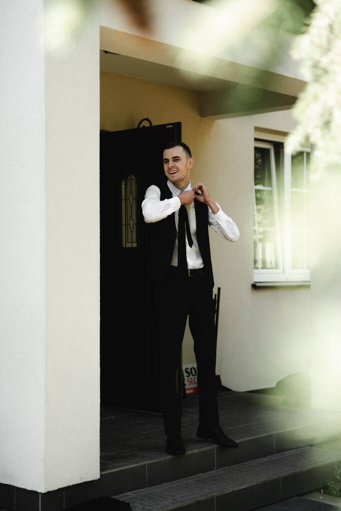 гонорари нареченого вдома. молодий чоловік збирається на весільний одяг. хлопець стоїть біля входу до будинку
 - Фото, зображення