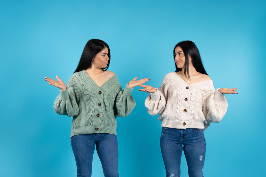 İkiz kadınlar birbirlerine bakarak avuçlarını iki yana açarlar. Mavi arka plandaki ilanınız için duygular. Yüksek kalite fotoğraf - Fotoğraf, Görsel
